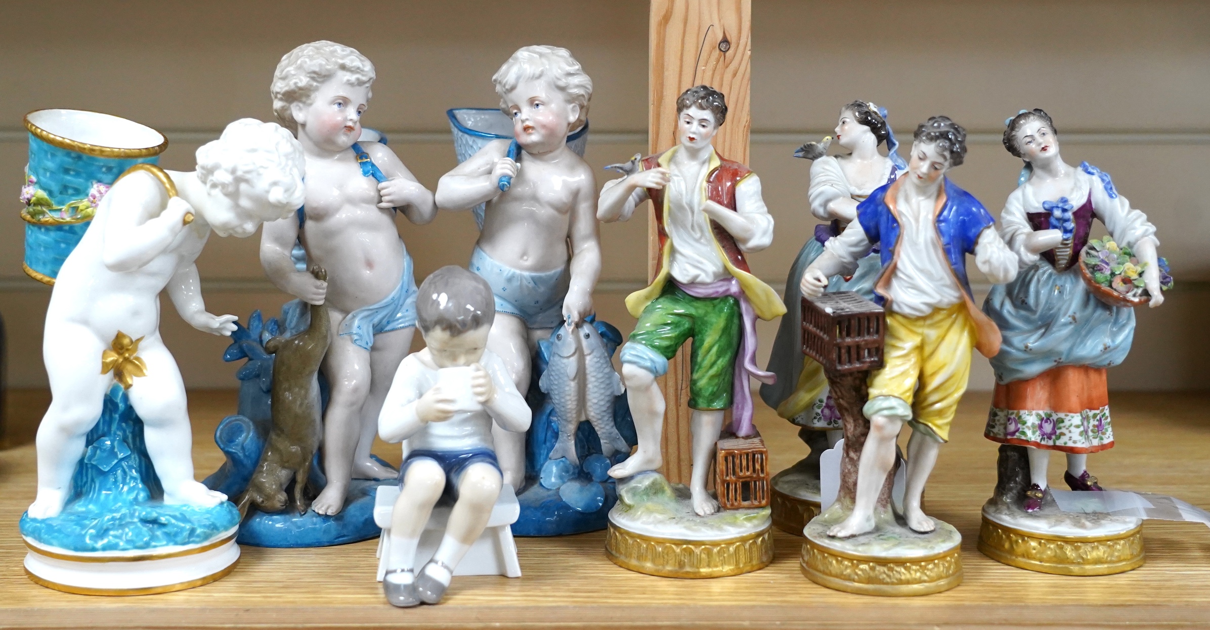 Three late 19th century porcelain putti spill vases and four smaller figurines, tallest 23cm high